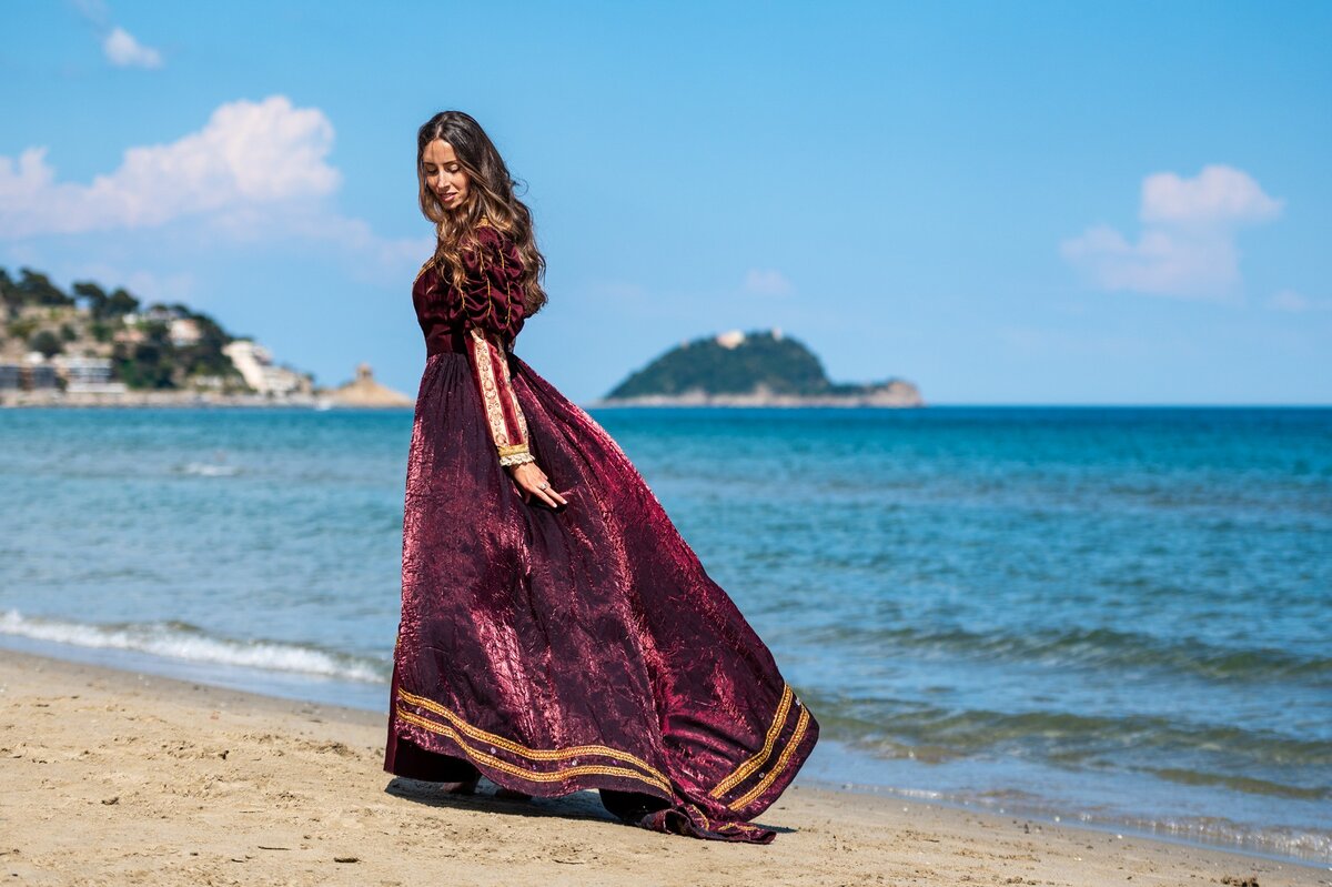 Donna con abito lungo bordeaux che cammina sulla spiaggia al mare