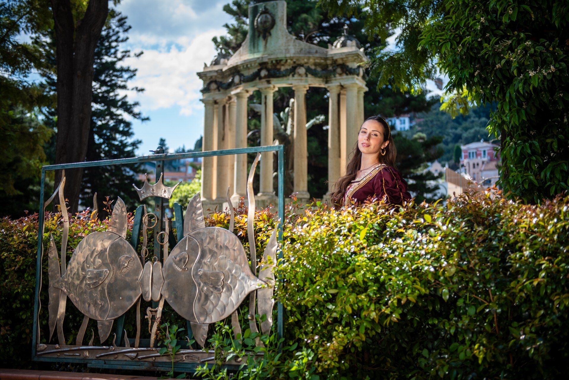 Donna in abito elegante vicino a monumento e cancellata artistica in giardino