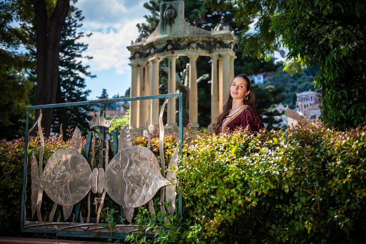 Donna in abito elegante vicino a monumento e cancellata artistica in giardino