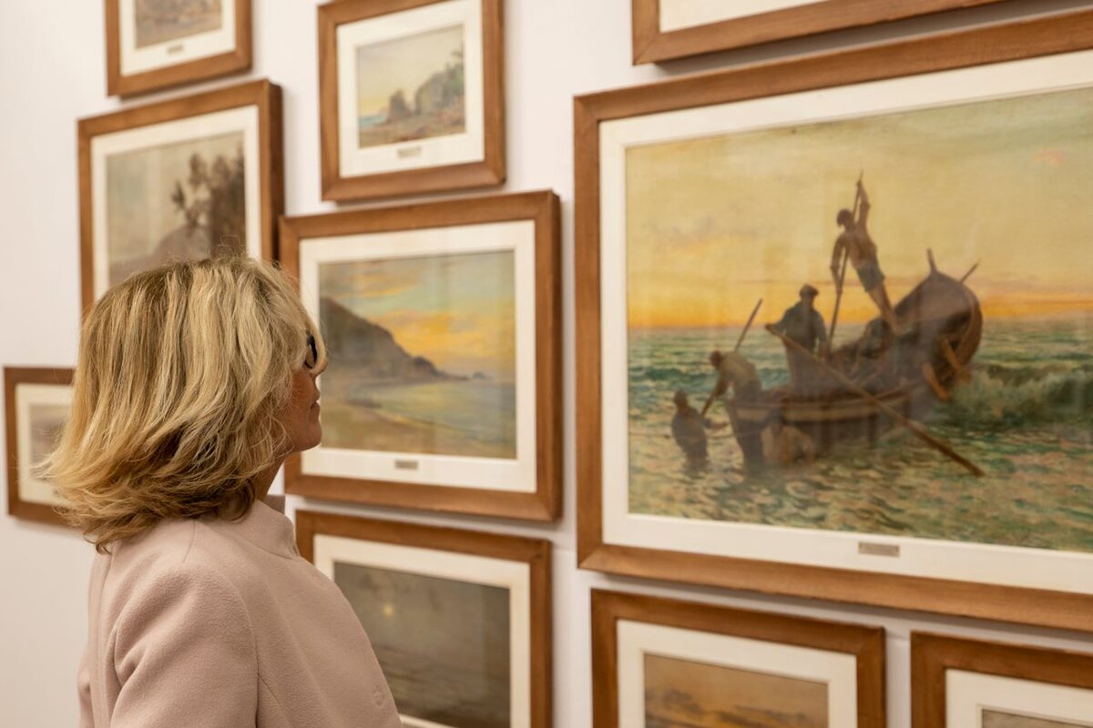 Frau betrachtet Gemälde mit Meereszenen in einer Kunstgalerie.