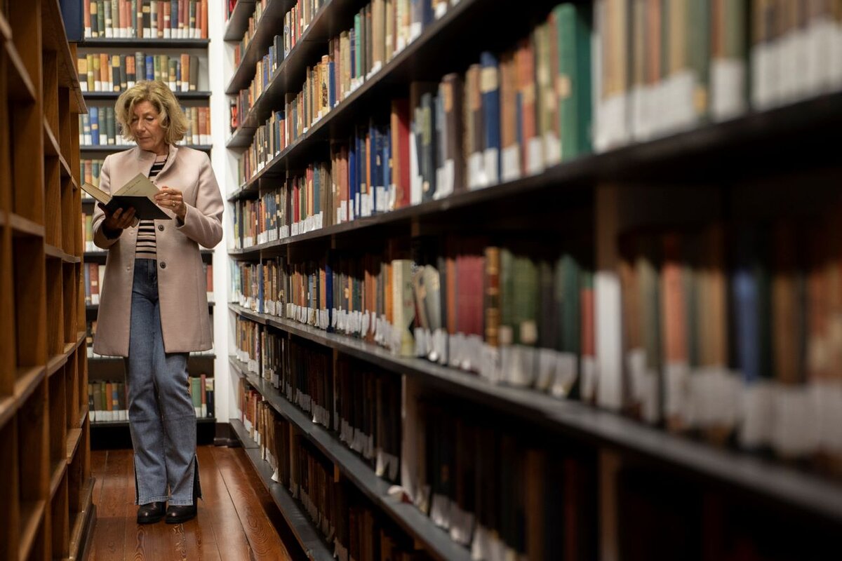 Woman reading a book between library shelves.